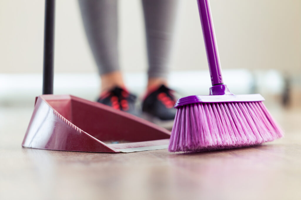 Close-up of young woman cleaning her flat with broom and collector at home.