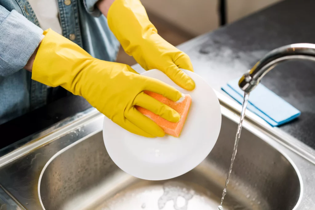 woman wearing gloves washing plates in a sink