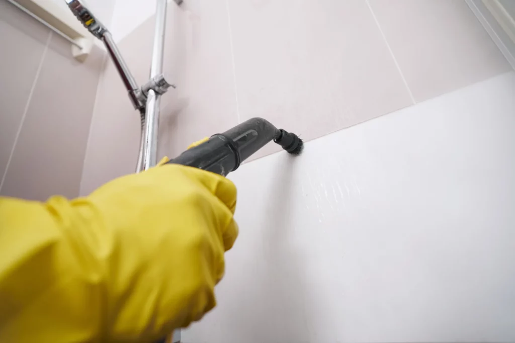Person wearing yellow gloves steam cleaning bathroom tile grout