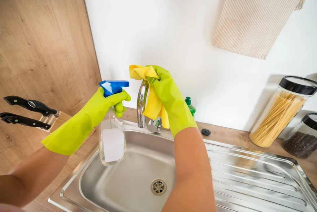 person wearing green rubber gloves to clean stainless steel sink