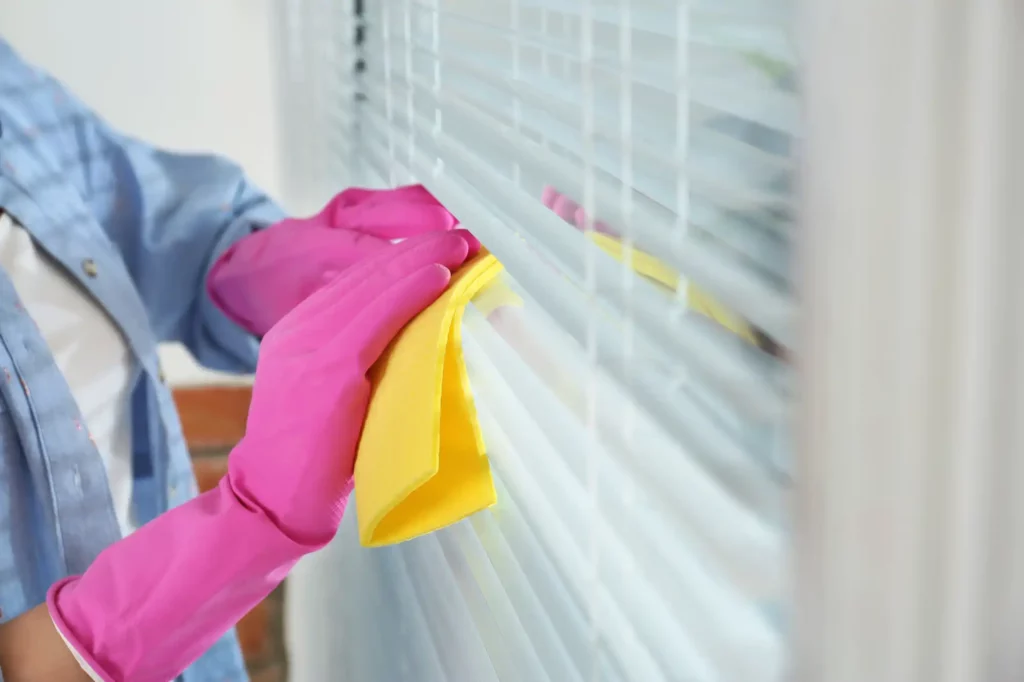 Person wearing pink rubber gloves cleaning blinds with a yellow microfibre cloth