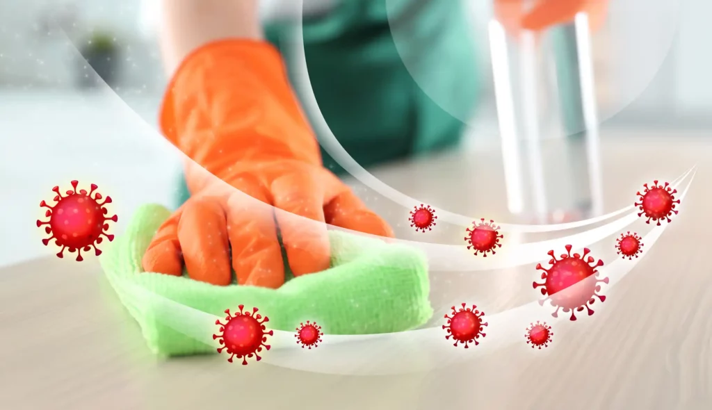 Person wearing orange rubber gloves using a green cloth and disinfectant to remove germs from surface