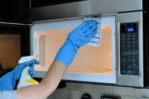 Person wearing blue rubber gloves to clean inside of microwave