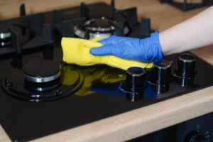 person wearing blue gloves using a yellow microfibre cloth to clean a gas stove hob